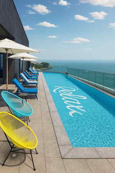 Rooftop pool with ocean view at Busan Hotel L7 Haeundae by Lotte Hotel, featuring lounge chairs, umbrellas, and a clear coastal skyline under sunny weather.