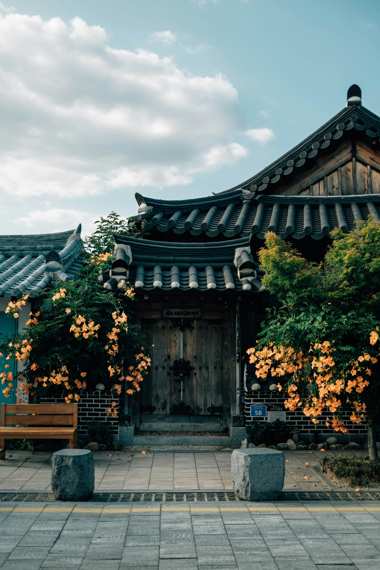 Traditional Korean wooden house with tiled roof and orange flowers at Namsangol Hanok Village in Seoul under a bright sky