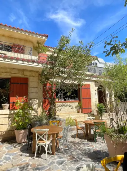 Outdoor cafe scene near Apgujeong Rodeo Street restaurants with stone terrace, wooden tables, and bright Mediterranean-style building.