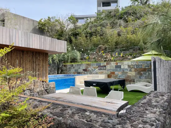 Outdoor poolside area at Bayhill Pool & Villa in Jeju with lounge chairs, greenery and stone walls
