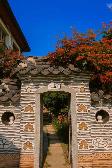 Entrance gate of a traditional Hanok alley near the Bukchon Oriental Culture Museum, with tiled roof and autumn leaves.