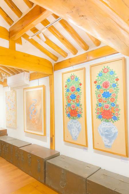 Interior of the Bukchon Oriental Culture Museum with traditional Korean Hanok beams and colorful folk paintings displayed on the wall.
