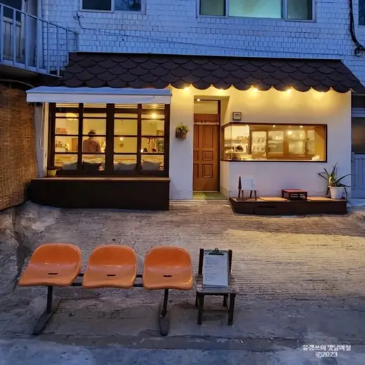 Evening exterior view of Gonggan Dabansa, a cozy Seoul cafe with warm lights and vintage seating.