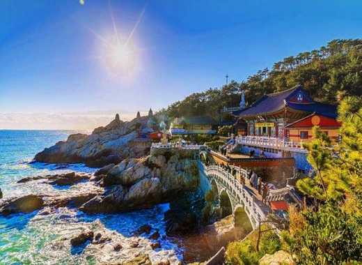 Haedong Yonggungsa Temple overlooking the blue ocean with autumn-colored trees along the rocky coastline in Busan, South Korea.
