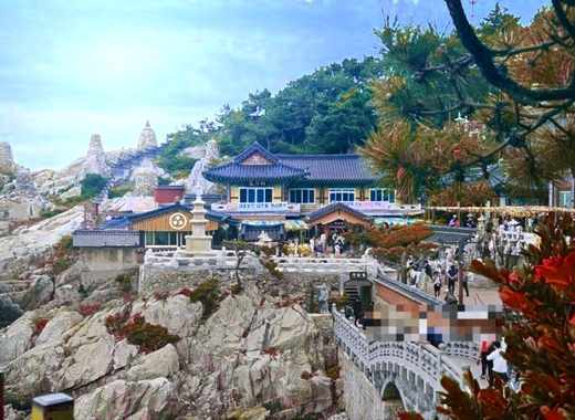 Haedong Yonggungsa Temple on a rocky seaside cliff with autumn-colored trees and a bright blue sky in Busan, South Korea.

