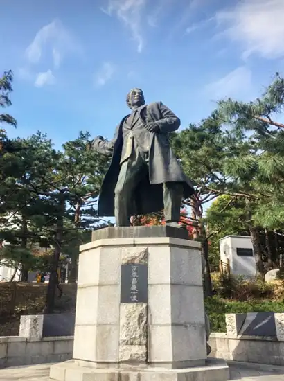 Statue monument at Hyochang Park honoring a Korean independence figure, surrounded by pine trees under a clear sky.
