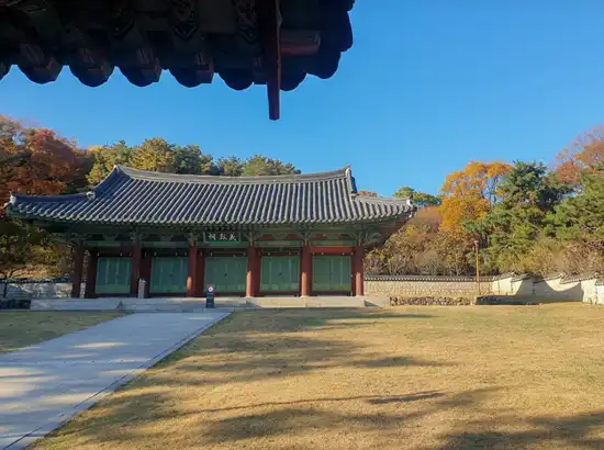 Traditional Korean royal-style shrine building at Hyochang Park, surrounded by autumn trees and a clear blue sky.