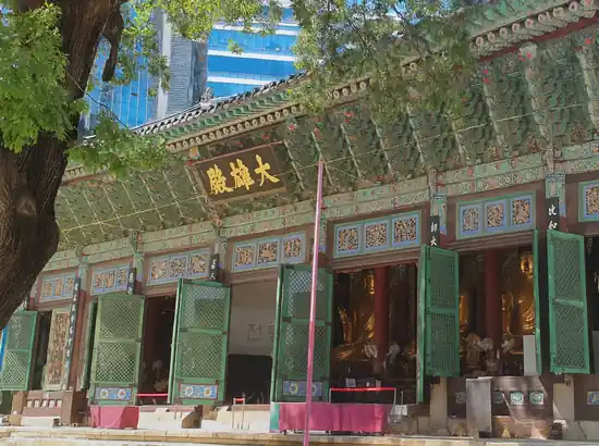 Insadong travel scene showing Jogyesa Temple’s main hall with open green doors, detailed dancheong patterns, and golden Buddha statues.