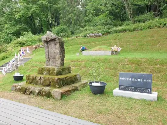 Memorial site at Mangu History Culture Park with stone monument and grassy hillside.