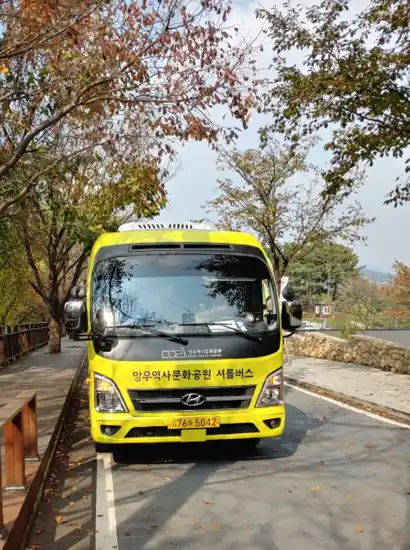 Free shuttle bus at Mangu History Culture Park parked along a tree-lined road in autumn.