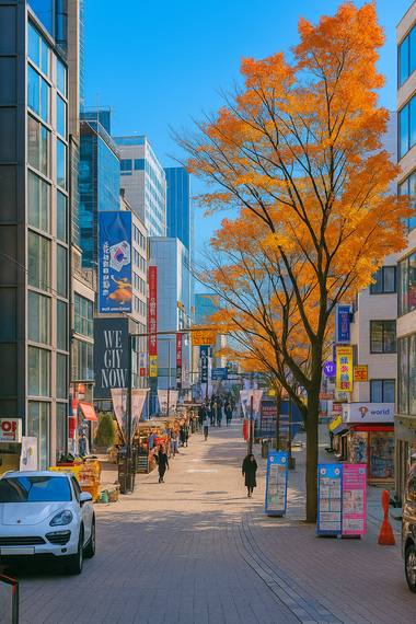 Autumn street view near Myeongdong Cathedral in Seoul, with shops, pedestrians, and clear blue sky.