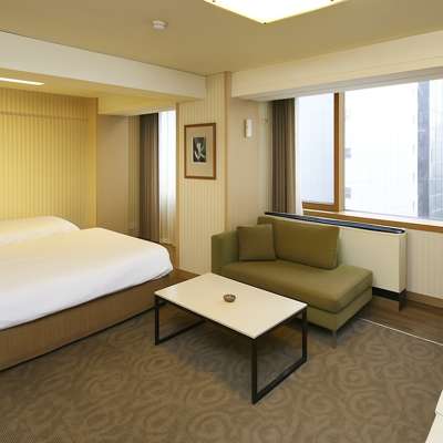 Bright interior of a guest room at Savoy Hotel Myeongdong in Seoul, showing a double bed, sofa, and large window with open curtains and natural daylight