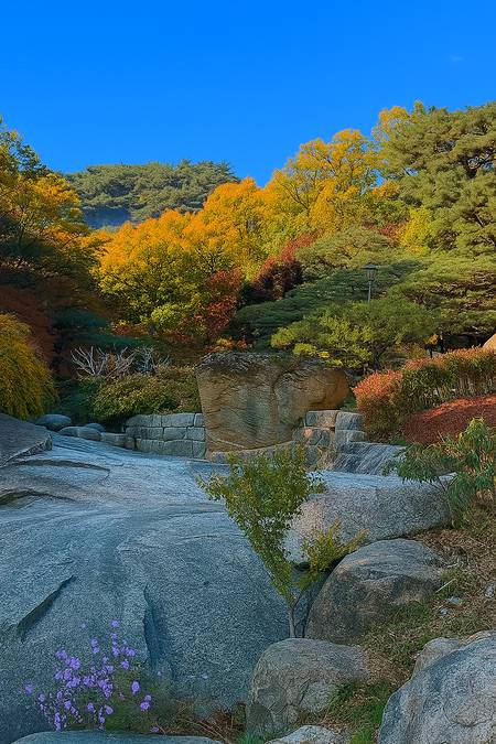 Autumn garden scenery at Seokpajeong Seoul, with colorful forest and stone terraces under a clear blue sky.
