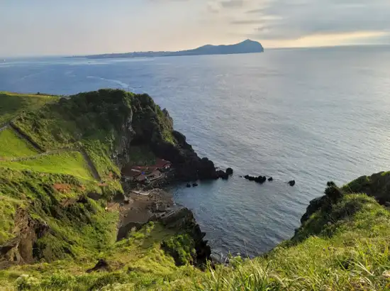 Coastal cliff and emerald sea captured during a Seongsan Ilchulbong sunrise trip, overlooking Jeju’s eastern coastline and the scenic village area below.
