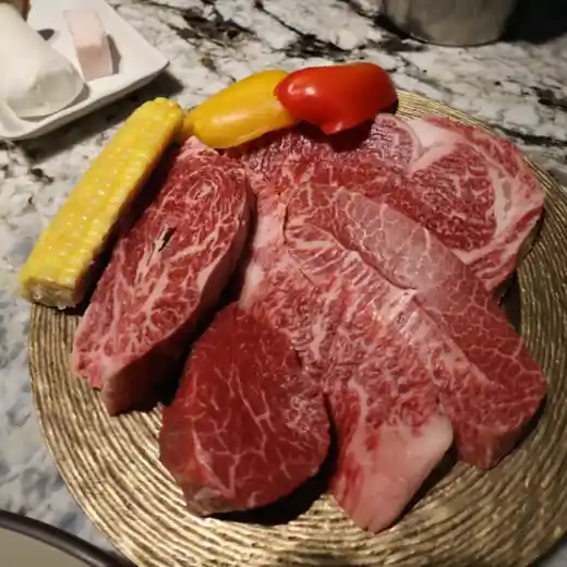 Premium Korean beef platter served at a restaurant, featuring marbled cuts, vegetables, and corn on a golden plate.