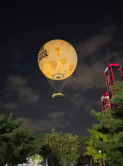 Night view of Seoul Dal in Yeouido, a tethered hot-air balloon floating above the park with city lights in the background.