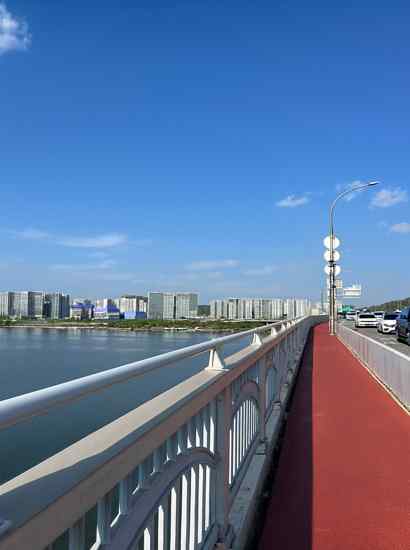 View from Gayang Bridge along the Seoul Dulle-gil 15 Course, showing a clear sky, the Han River, and the walking path toward western Seoul