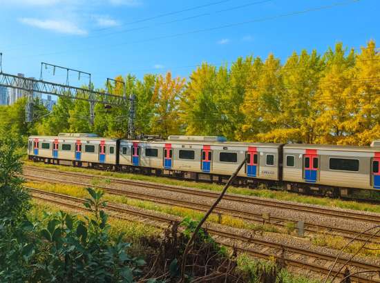Railway scene along the Seoul Dulle-gil 13 Course Anyangcheon Upper Stream, showing a commuter train passing through green and slightly autumn-colored trees.