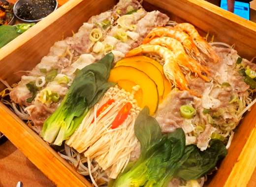 Seoul food steamed platter with beef, vegetables, and shrimp served in a wooden steam tray
