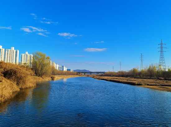 Riverside scenery along Seoul Trail Course 8 Jangji-Tancheon with blue sky and calm water.
