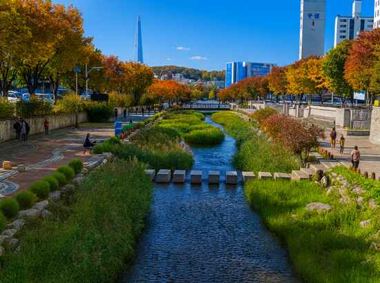 Scenic stream walkway on Seoul Trail Course 8 Jangji-Tancheon with clear blue sky and autumn trees.
