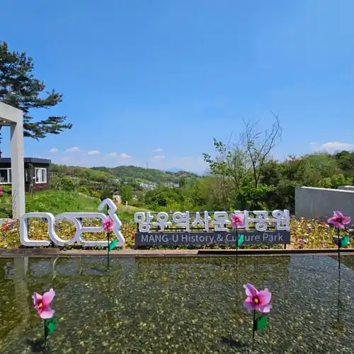 Entrance view of Mang-u History and Culture Park along Seoul Trail Section 4, with flowers, clear blue sky, and surrounding greenery.