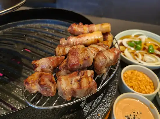 Grilled pork belly served on a hot plate at Ttukseom Hangang Park, with dipping sauces and side dishes.