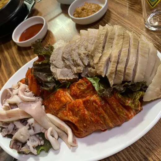 A plate of Korean bossam with boiled pork slices, kimchi, and squid served near Yanghwa Hangang Park in Seoul.
