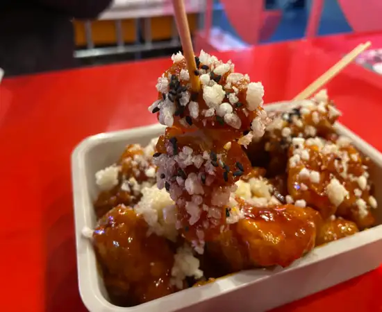 Korean crispy sweet chicken snack served at Gwanghwamun Market, topped with puffed rice and sesame seeds.