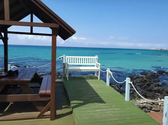 Ocean-view wooden deck in Jeju with a white bench and turquoise sea, Jeju accommodation area selection planning reference