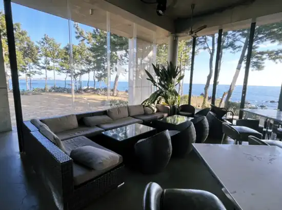 Ocean-view café interior in Jeju with large windows and coastal pine trees, Jeju City vs Seogwipo base planning reference