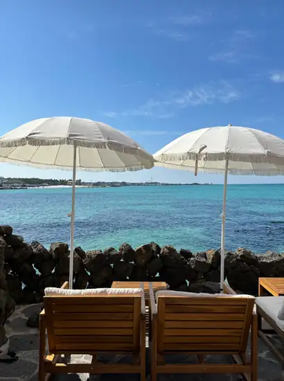 Turquoise sea view in Jeju with two white umbrellas and wooden lounge chairs by a lava rock wall, Jeju City vs Seogwipo base planning reference