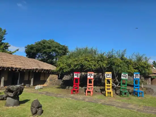 Main sign area and traditional houses inside Jeju Folk Village, included as part of the Jeju Folk Village entrance fee experience.
