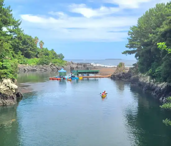 Kayaking at Soesokkak Estuary on the Jeju Seogwipo travel course, with clear water, lava cliffs, and a scenic opening toward the ocean.