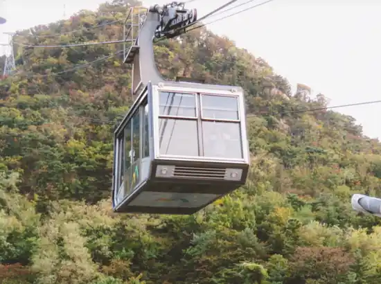 Namsan Cable Car cabin in motion above the forested hillside, classic ride toward Namsan, namsan cable car ticket price guide