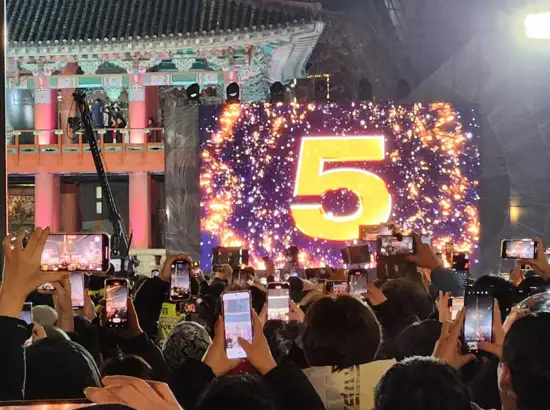 Countdown screen showing number 5 during the New Year Bell-Ringing Ceremony at Boshingak in Seoul, with visitors holding phones to record the moment