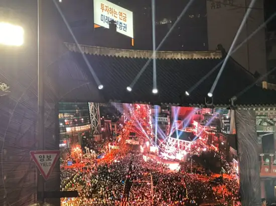View of the large crowd gathered at Boshingak during the New Year Bell-Ringing Ceremony in Seoul, with stage lighting and street screens illuminating the event at night