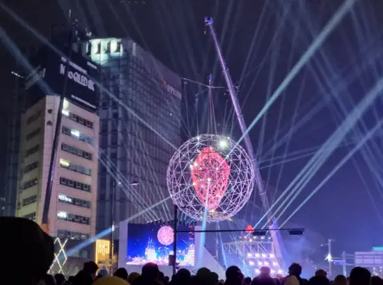 Light sphere installation above the stage during the New Year Bell-Ringing Ceremony in Seoul, with night lights and crowd watching the performance