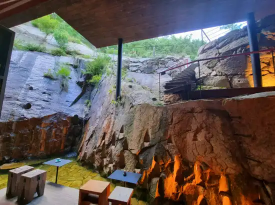 Natural valley seating area at a café near Seoul Dullegil Course 18, with carved rock walls, flowing water, and wooden tables.