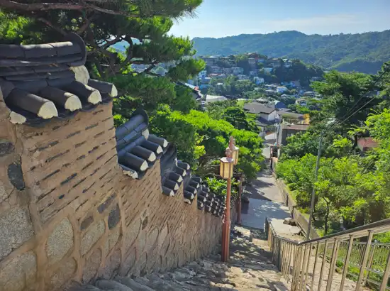Scenic descending walkway along Seoul Dullegil Course 18 overlooking Pyeongchang-dong village and surrounding green mountains.
