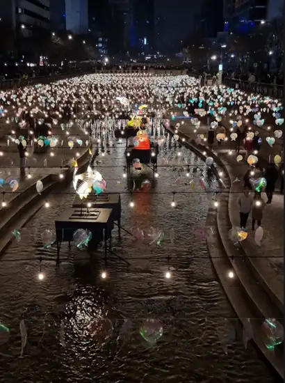 Winter light festival featuring floating lantern displays along Cheonggyecheon Stream in Seoul, with visitors walking beside illuminated pathways