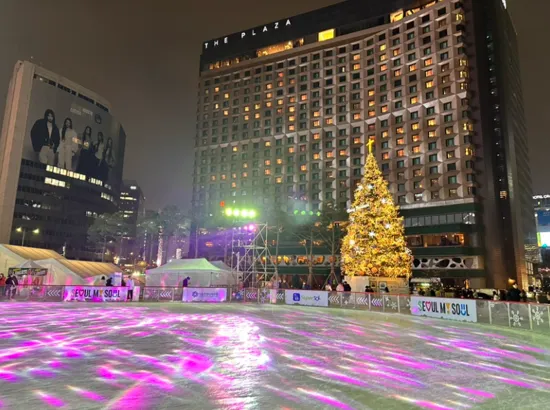 Night view of the Seoul Plaza Ice Rink with a large Christmas tree and illuminated rink surface in front of The Plaza Hotel