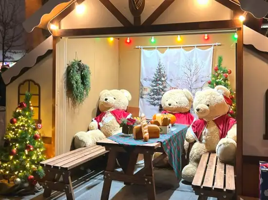 Christmas-themed bear photo zone at the Seoul Winter Festa, featuring teddy bears sitting at a decorated table with holiday lights and trees.