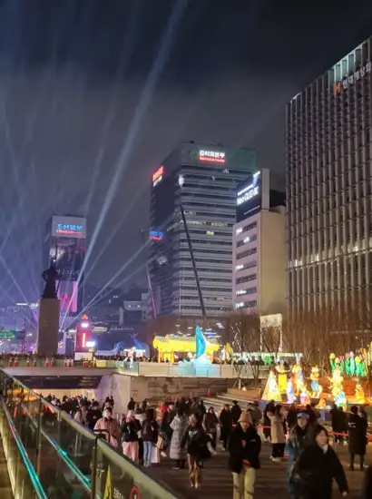 Night view of Gwanghwamun area during Seoul Winter Festa, with illuminated installations along the stream and people walking through the decorated pathways