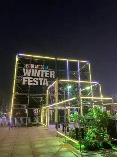 Main entrance installation of the Seoul Winter Festa at night, illuminated with neon frame lights and signage in an open plaza.