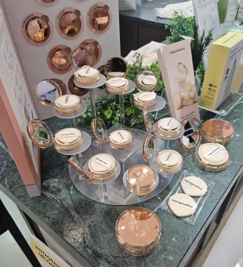 K-beauty cushion foundation display at DDP, photographed for the seoulcon 2025 schedule, showing multiple compact cases on a stand.