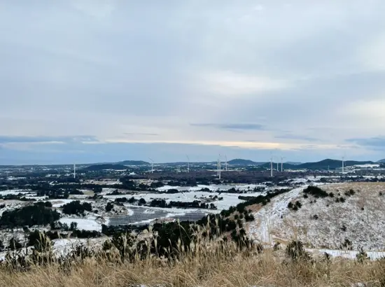 Winter landscape of Yongnuni Oreum with snow-covered fields and wind turbines in eastern Jeju.