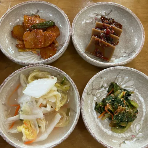 Haebangchon restaurants in Seoul side dishes served in small bowls (kimchi, acorn jelly, cabbage soup, seasoned greens).