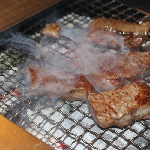 Korean BBQ galbi grilling on a charcoal mesh grill with smoke rising