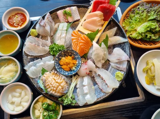 Assorted sashimi table setting at Jinju Restaurant, served with dipping sauces, lettuce, and side dishes.